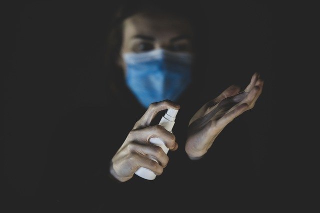 person spraying hand sanitizer on hands and wearing a mask